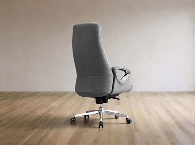 A modern gray leather office chair with a high back, silver five-star base, and black casters, shown from the rear on a light wood floor against a neutral beige wall.
