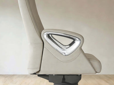 A close-up side view of a modern beige leather office chair with a prominent chrome-trimmed triangular armrest detail, set against a neutral beige wall and light wood floor.