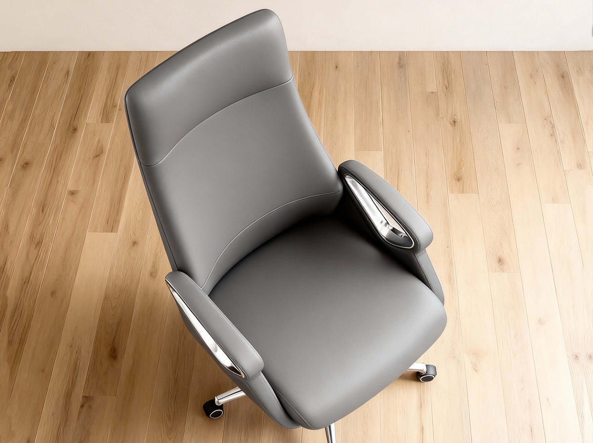 A gray upholstered office chair with chrome armrests and a five-wheel base, photographed from above on a light wood floor against a white wall.
