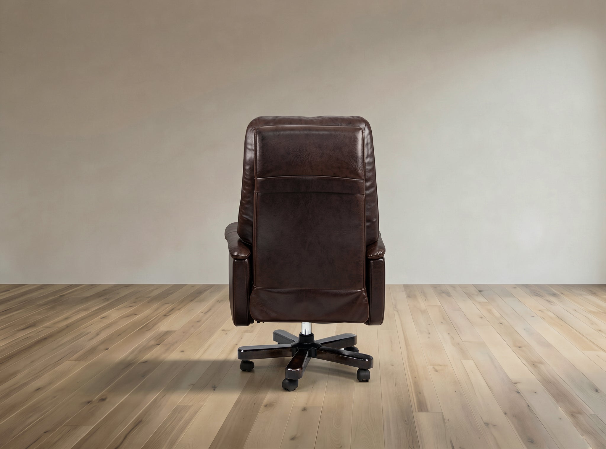 A dark brown leather office chair with a high back and black wheeled base, photographed from the rear in a minimalist room with light wood flooring and a beige wall.