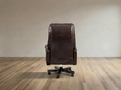 A dark brown leather office chair with a high back and black wheeled base, photographed from the rear in a minimalist room with light wood flooring and a beige wall.