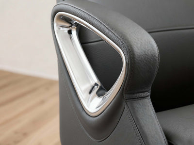 Close-up of a dark gray leather office chair armrest featuring a polished chrome triangular accent frame.
