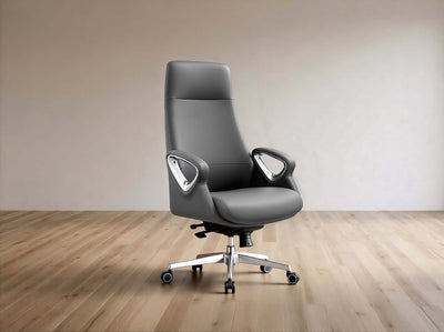 A modern gray leather office chair with a high back, curved armrests, and a chrome five-star base with casters, set against a minimalist beige wall and light wood floor.