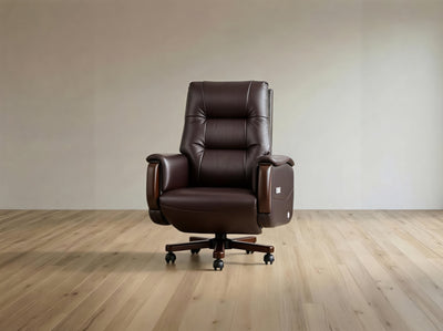 A dark brown leather office chair with a high back, padded armrests, and a five-star wheeled base, shown in a minimalist room with light wood flooring and a beige wall.